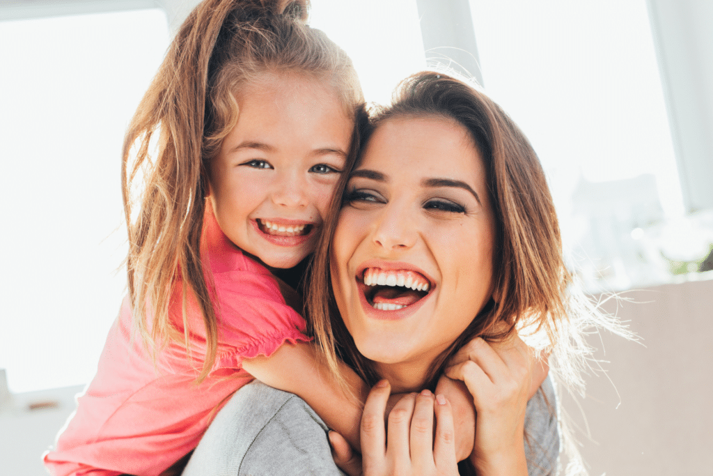 Mother and young toddler girl with healthy smiles hugging closely indoors