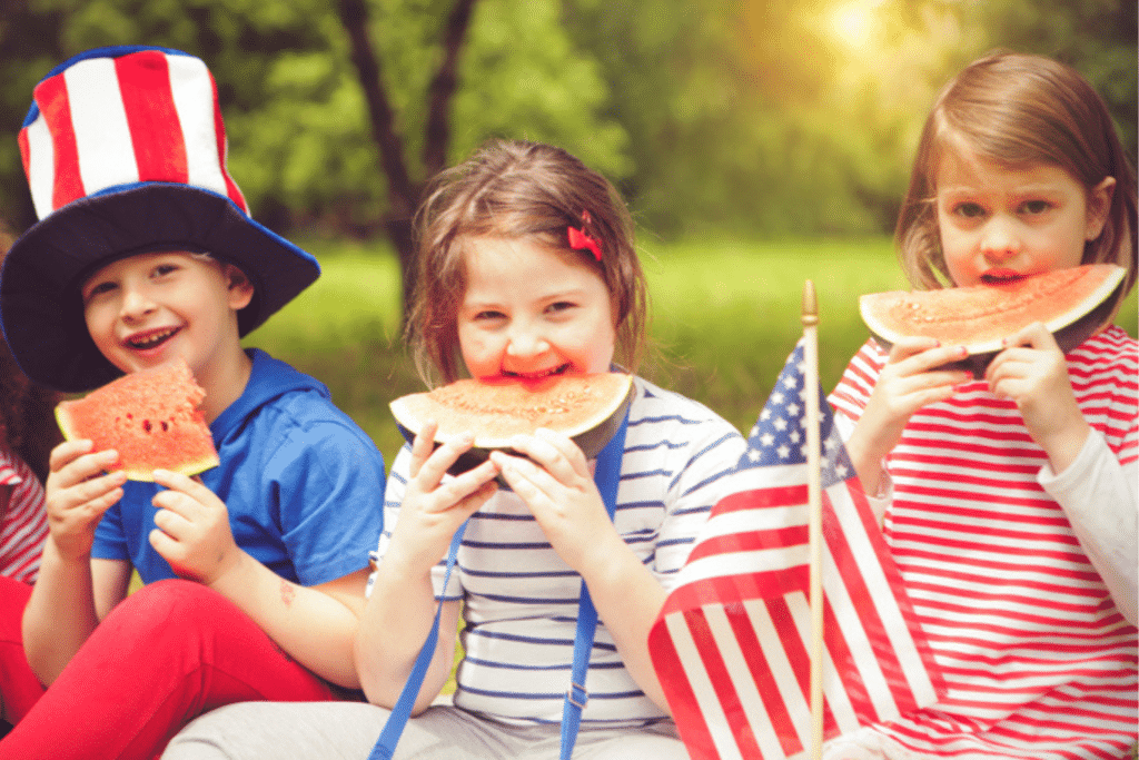Young children smiling while eating watermelon slices outdoors