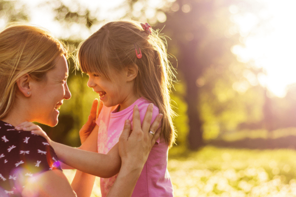 Smiling mother hugging her young daughter outdoors in a sunlit park